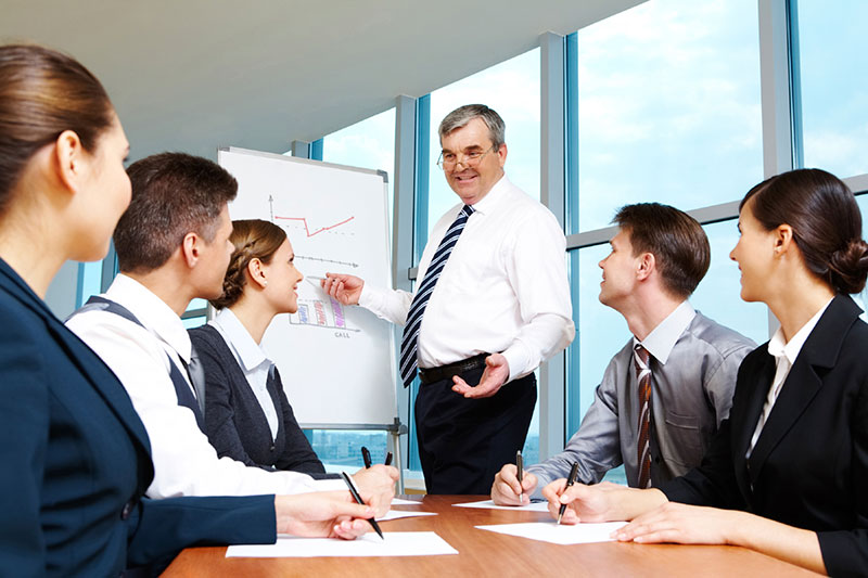 Elderly boss pointing at whiteboard and looking at managers during presentation